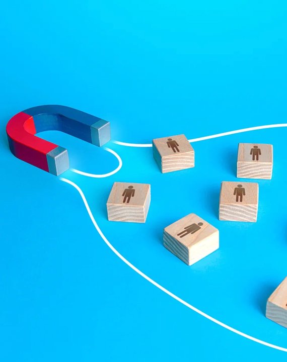 Imán atrayendo bloques de madera con íconos de personas sobre fondo azul, simbolizando la generación de leads.